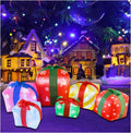 Cluster of colorful inflatable gift boxes glowing in front of a snowy village scene