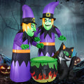 Inflatable pair of green witches in purple hats stirring a glowing cauldron with a black cat