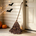 Rustic witch's broom leaning by a front door with paper bats on the wall