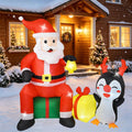 Inflatable Santa sitting on a gift box beside a waving penguin in front of a house