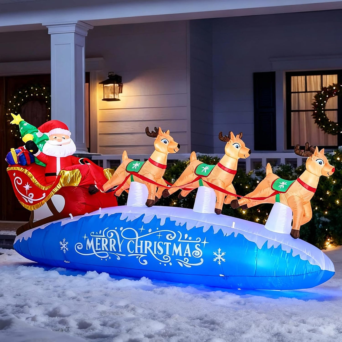 Inflatable Santa in a red sleigh pulled by reindeer on a blue Merry Christmas base in front of a porch