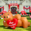Inflatable brown bear lying on a lawn holding a red Happy Valentine's Day heart