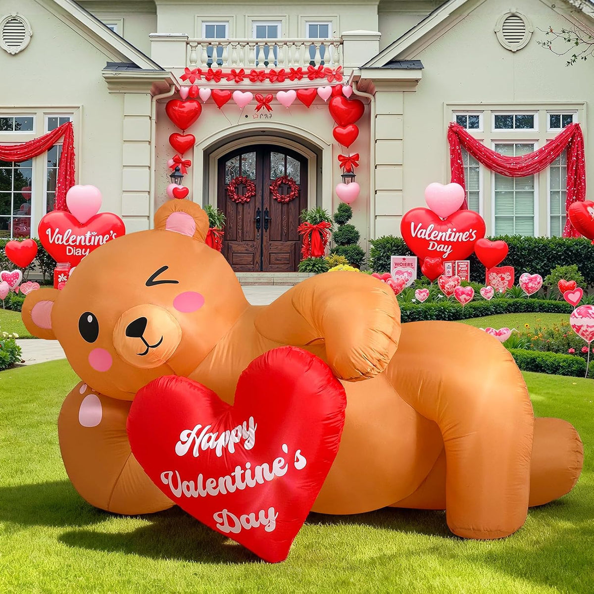 Inflatable brown bear lying on a lawn holding a red Happy Valentine's Day heart