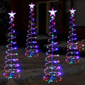 Four glowing multicolor spiral light trees with white star toppers in a dark yard