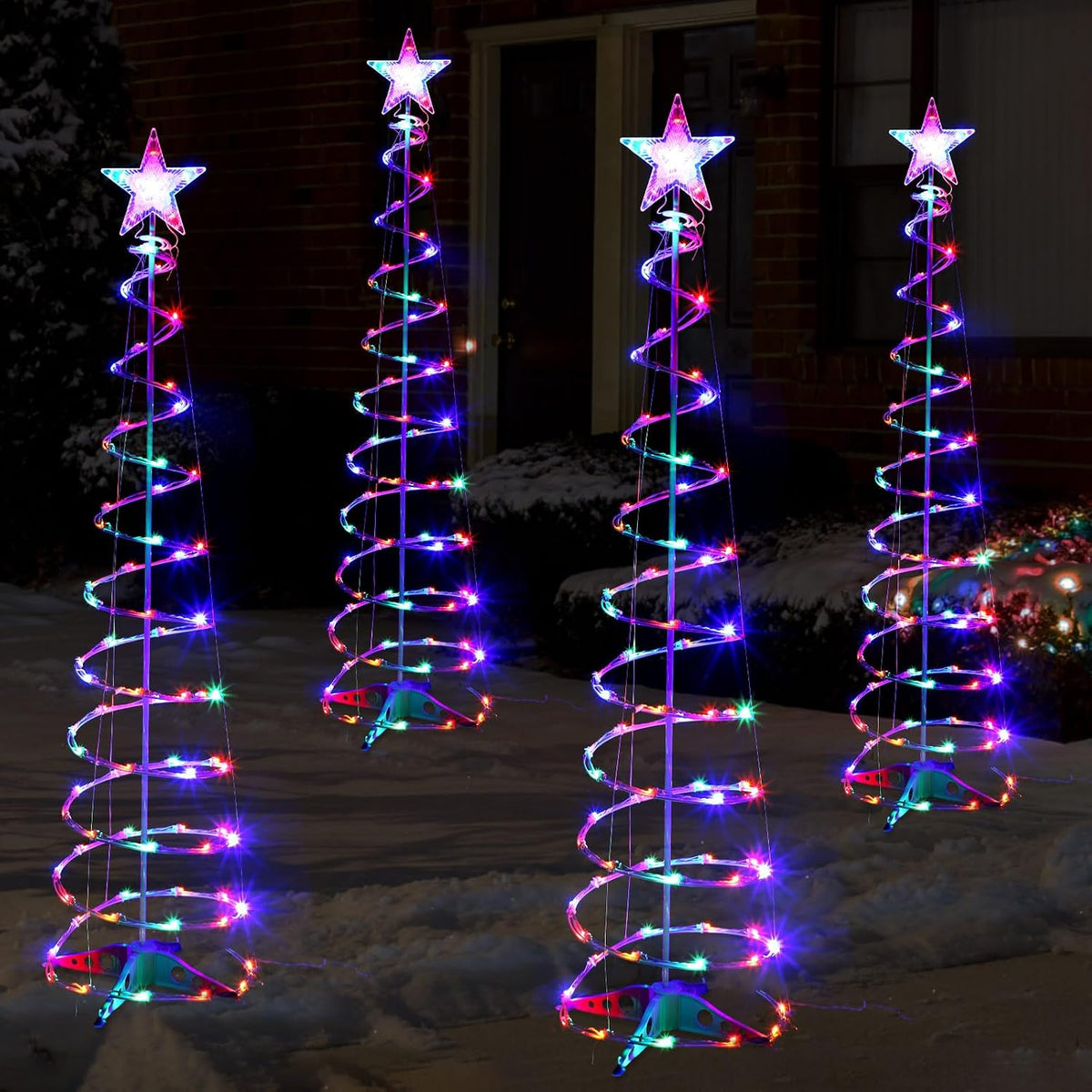 Four glowing multicolor spiral light trees with white star toppers in a dark yard