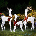 Three white lighted reindeer with red bows glowing on a lawn at night